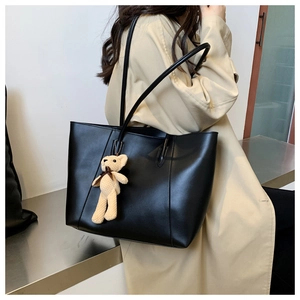 Detail of black tote bag with cute knit bear charm worn over a beige trench coat