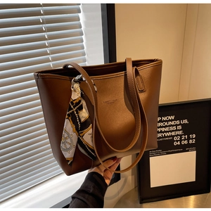 Detailed shot of brown leather tote bag with elegant silk scarf on handle and embossed logo