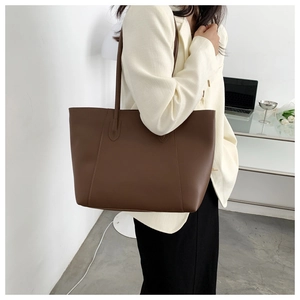 Detail view of a dark coffee leather tote bag with fine stitching in an office setting