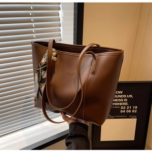 Detail view of brown leather tote bag featuring a decorative scarf and gold logo engraving