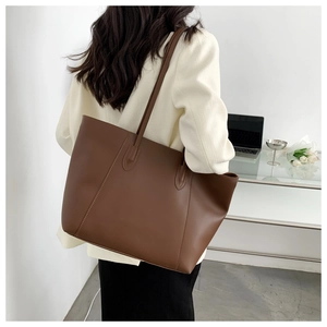 Detail of a large brown tote bag showing matte faux leather texture and sturdy strap seams