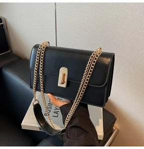 Detail of minimalist black crossbody bag showing gold metal chain and twist lock clasp