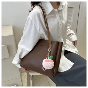 Detail of dark brown leather tote bag with brand logo and peach plush charm on strap