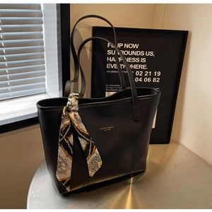 Detail of black faux leather tote bag with elegant printed silk scarf on the strap