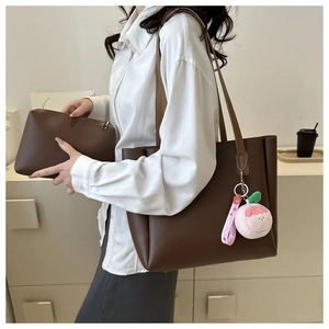 Detail of dark brown leather tote bag set with a peach plush charm on a model