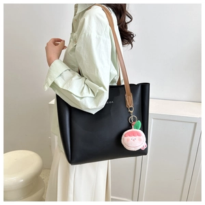 Close-up of black tote bag with brown straps and a cute peach plush charm pendant