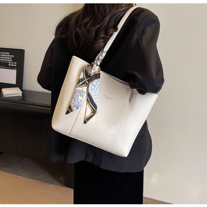 Detail of cream leather tote bag featuring a decorative silk scarf and fashion slogan print