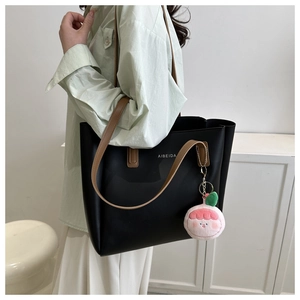 Detail of black leather tote bag with brown straps and cute pink plush charm accessory