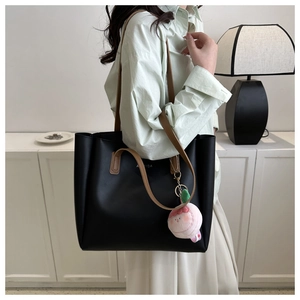 Detail of black tote bag with brown straps and a pink peach plush charm decoration