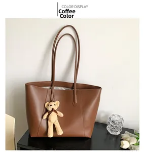 Close-up of brown faux leather tote bag with decorative bear pendant on table