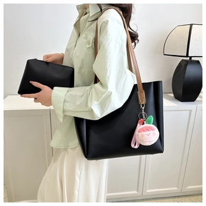 Close-up of black tote bag with peach plush charm and matching small pouch bag
