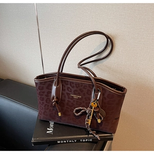 Détail d'un cabas léopard avec breloque clé en métal sur des livres noirs et mur beige