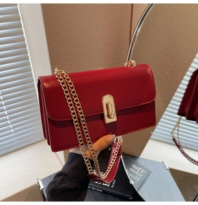 Detail of red leather shoulder bag with gold chain strap and metal turn-lock closure