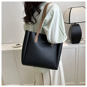 Detailed side view of large black matte tote bag with contrast brown leather handles
