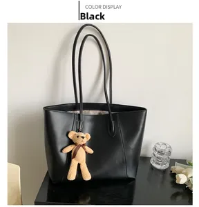 Detail of a black large tote bag with synthetic leather texture and a small bear charm