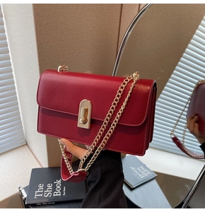 Macro view of dark red shoulder bag featuring elegant gold twist lock and chain strap