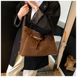 Macro shot of dark brown suede tote bag featuring adjustable leather straps and gold buckle