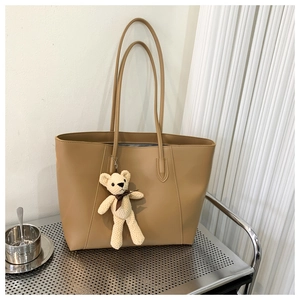 Detail of khaki tote bag with slender straps featuring a cute cream knit teddy bear pendant