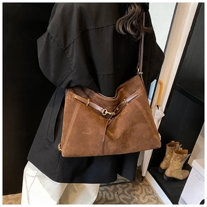 Detail view of the large dark brown suede tote bag worn by a model in a minimalist setting
