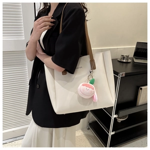 Detail of a cream tote bag with brown straps and a peach plush charm on a model