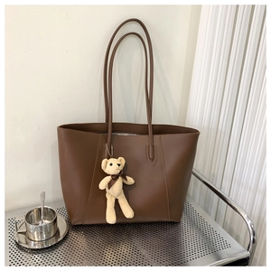 Detail view of large brown faux leather tote bag with a beige bear plush pendant