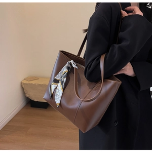 Detail of dark brown leather tote bag featuring a decorative nautical silk scarf on handle