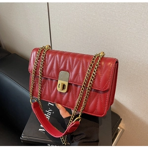 Detail of red quilted leather crossbody bag with V-shaped stitching and gold chain