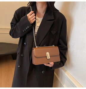 Brown leather crossbody bag with golden chain strap worn over a black classic coat