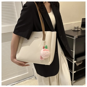 Detail of a beige tote bag with brown straps and a pink peach plush charm decoration