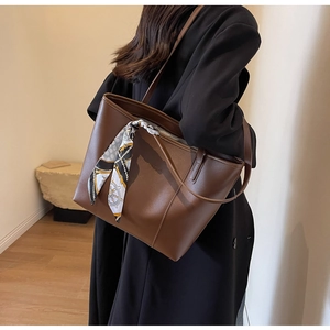 Detail view of brown faux leather tote bag with elegant silk scarf on the handle