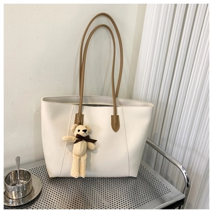 Close-up of cream tote bag with brown handles and a cute plush bear charm on a metal desk