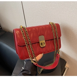 Detail of red V-quilted faux leather crossbody bag with golden twist lock and chain strap