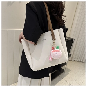 Detail of white leather tote bag with brown straps and cute pink peach plush charm