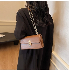 Detail of brown vintage flap bag with gold clasp and chain strap worn by a model