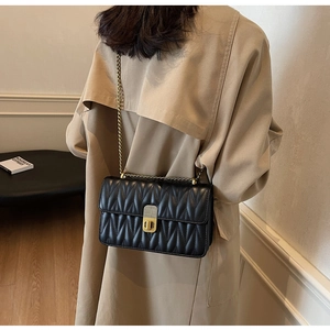 Close-up of black quilted crossbody bag with gold chain and metal twist lock on model