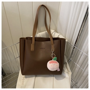 Detail of a brown tote bag featuring a plush pink peach charm and silver metal basket display