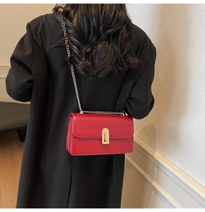 Detail of red glossy leather shoulder bag with gold chain strap on black blazer