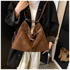 Detail of a large brown suede tote bag featuring a gold buckle and long tassel accents