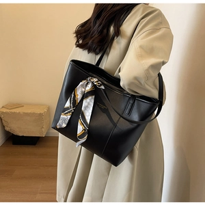Close-up of black leather tote bag with a patterned silk scarf on a model in a beige coat