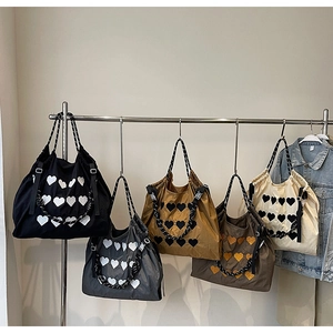 Detail view of five nylon tote bags with heart patterns hanging on a metal rack