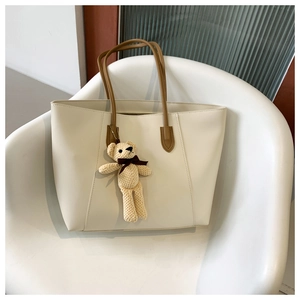 Detail of cream tote bag featuring a cute teddy bear charm and brown leather straps
