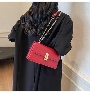 Detail of red leather shoulder bag with gold twist lock on black coat background