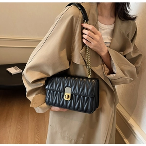 Detail of black quilted leather shoulder bag with gold chain strap and metal lock clasp