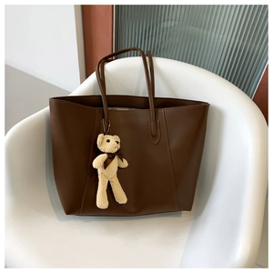 Detailed view of brown PU leather tote bag with a cute plush bear charm on a chair