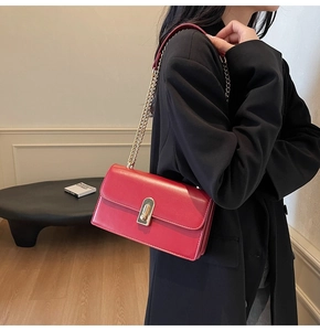 Close-up of red leather rectangular shoulder bag with gold chain and metal clasp detail