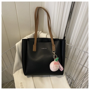 Detail of black leather tote bag with brown straps and pink peach plush charm in metal basket