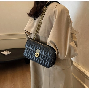 Close-up of black quilted matelassé leather texture and gold chain strap on shoulder bag