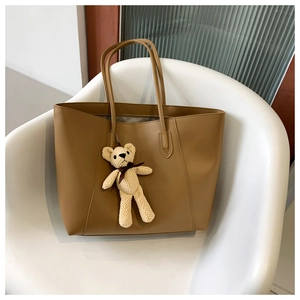 Detail view of large khaki tote bag with plush bear charm on a minimalist chair