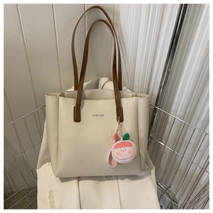 Close-up of minimalist cream tote bag with brown handles and a plush peach charm detail