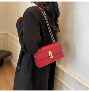 Detail of red leather bag with gold clasp and chain strap on black blazer